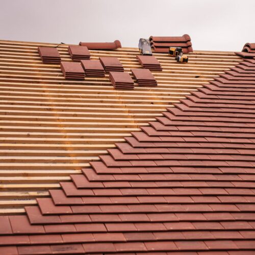 Partial installation of a terracotta tile roof on a building in progress.