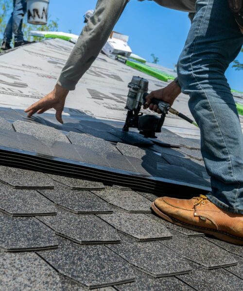 Roofer using nail gun for shingle installation on residential roof.